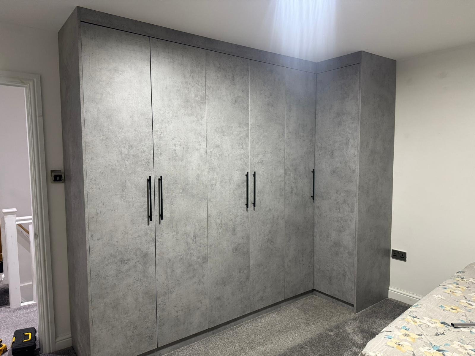 Bespoke corner wardrobe with concrete-effect panels and black bar handles